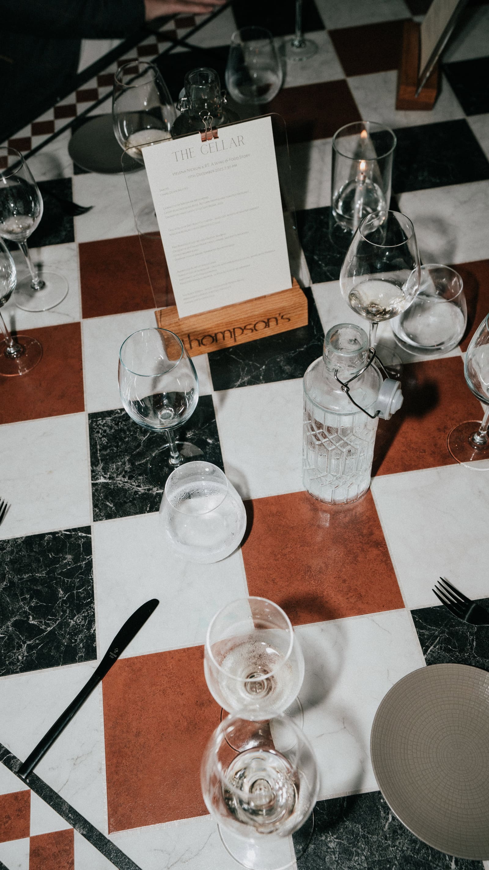 A Thompson’s menu card among wine glasses on the chequered marble table in The Cellar