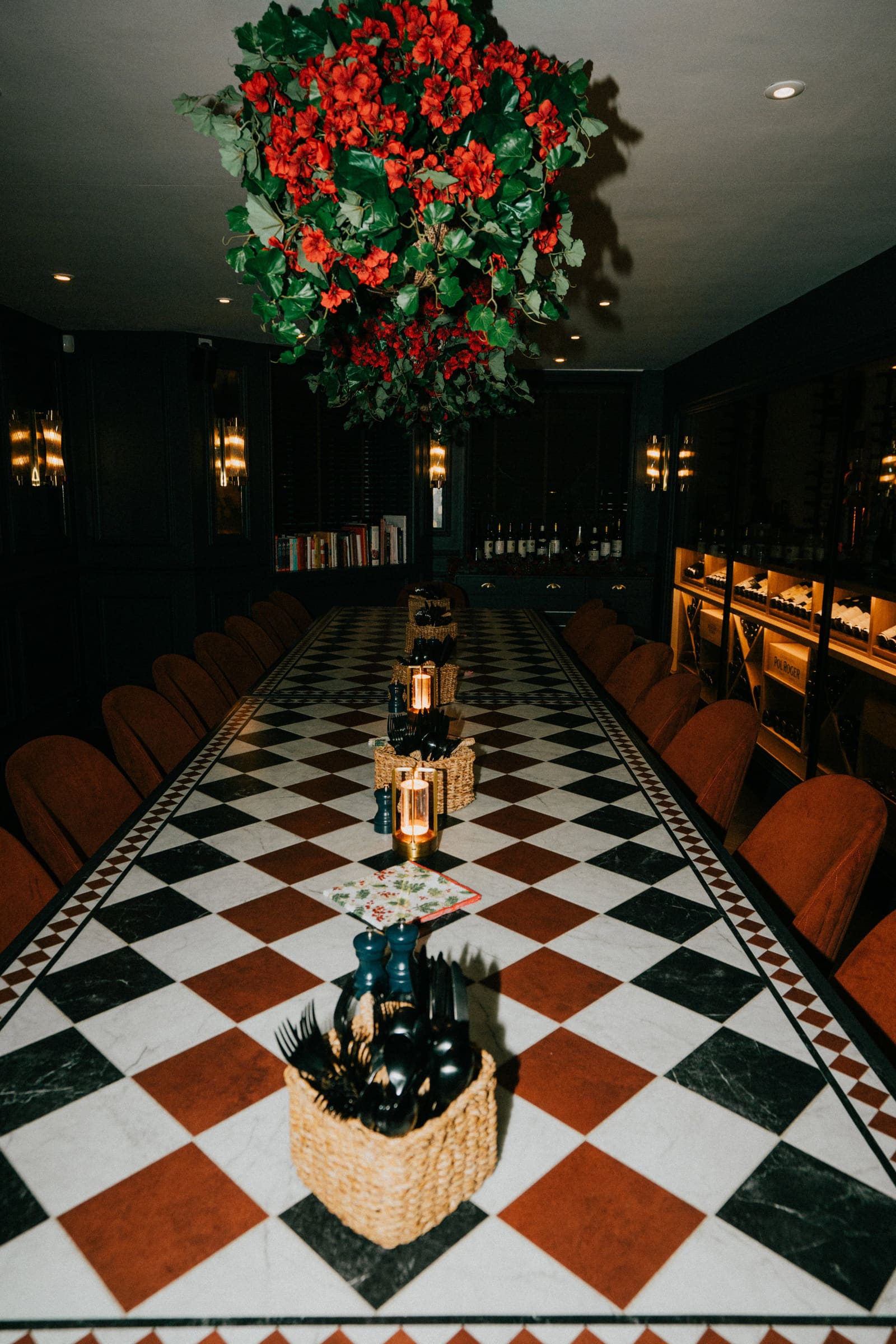 The long table in The Cellar, chequered marble, orange chairs and a chandelier of red flowers