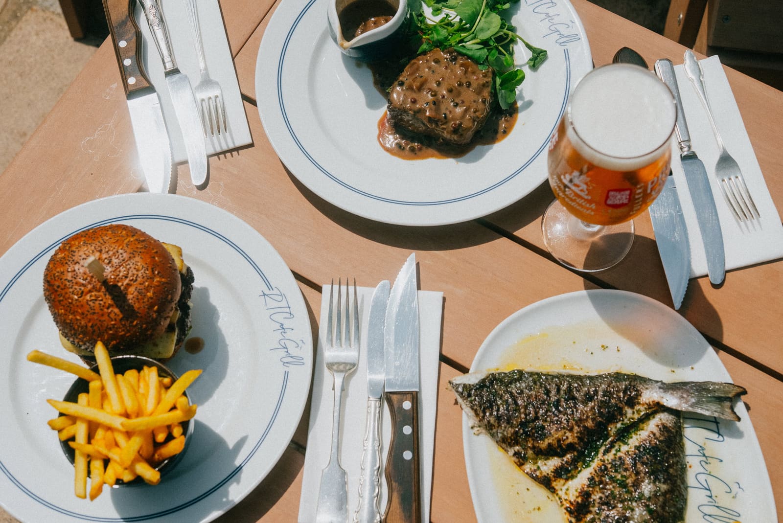 Steak au poivre, a burger and chips and a grilled bream on RT Café Grill plates, seen from above