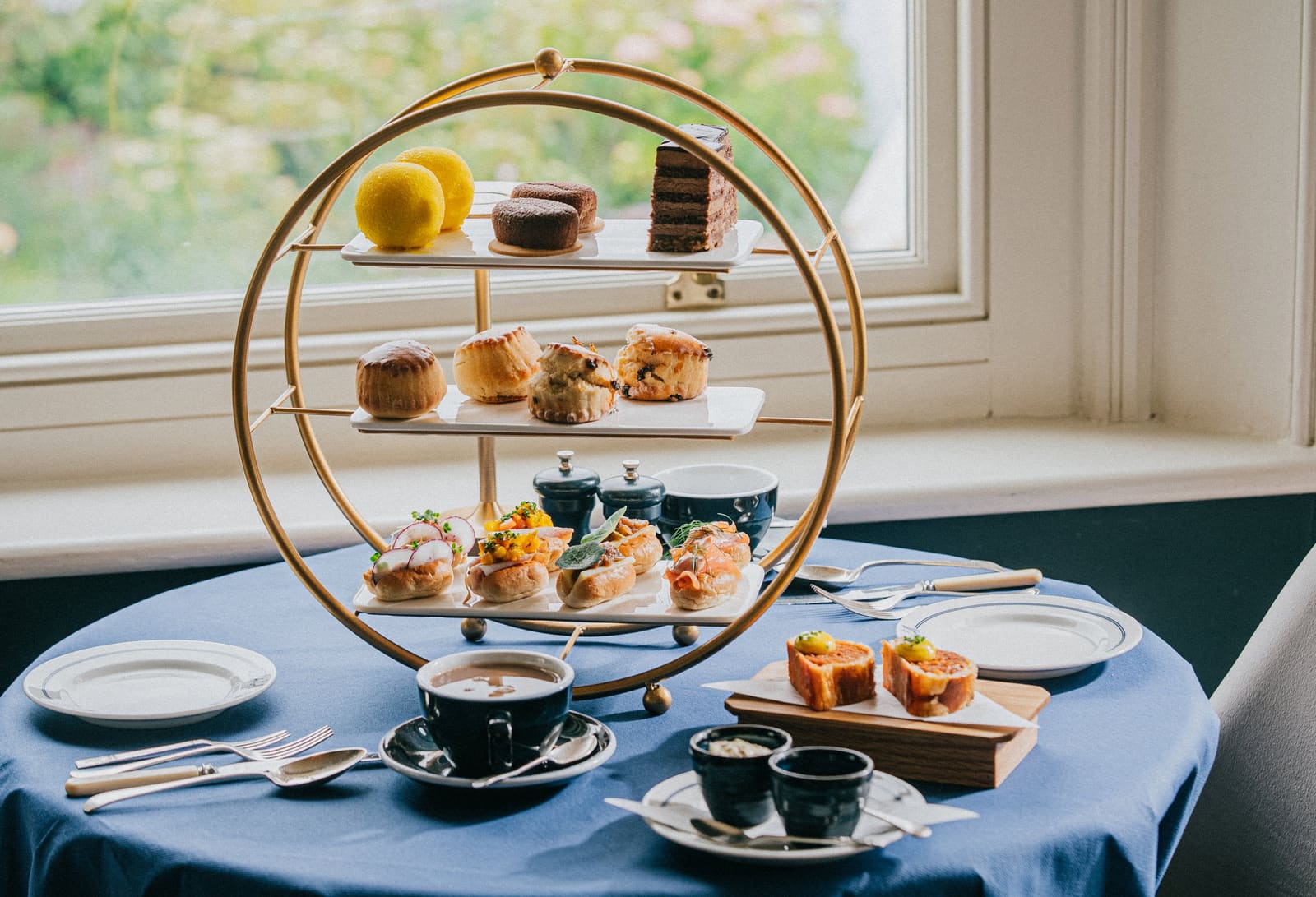 The afternoon tea stand on a blue tablecloth by the window, a pot of tea poured