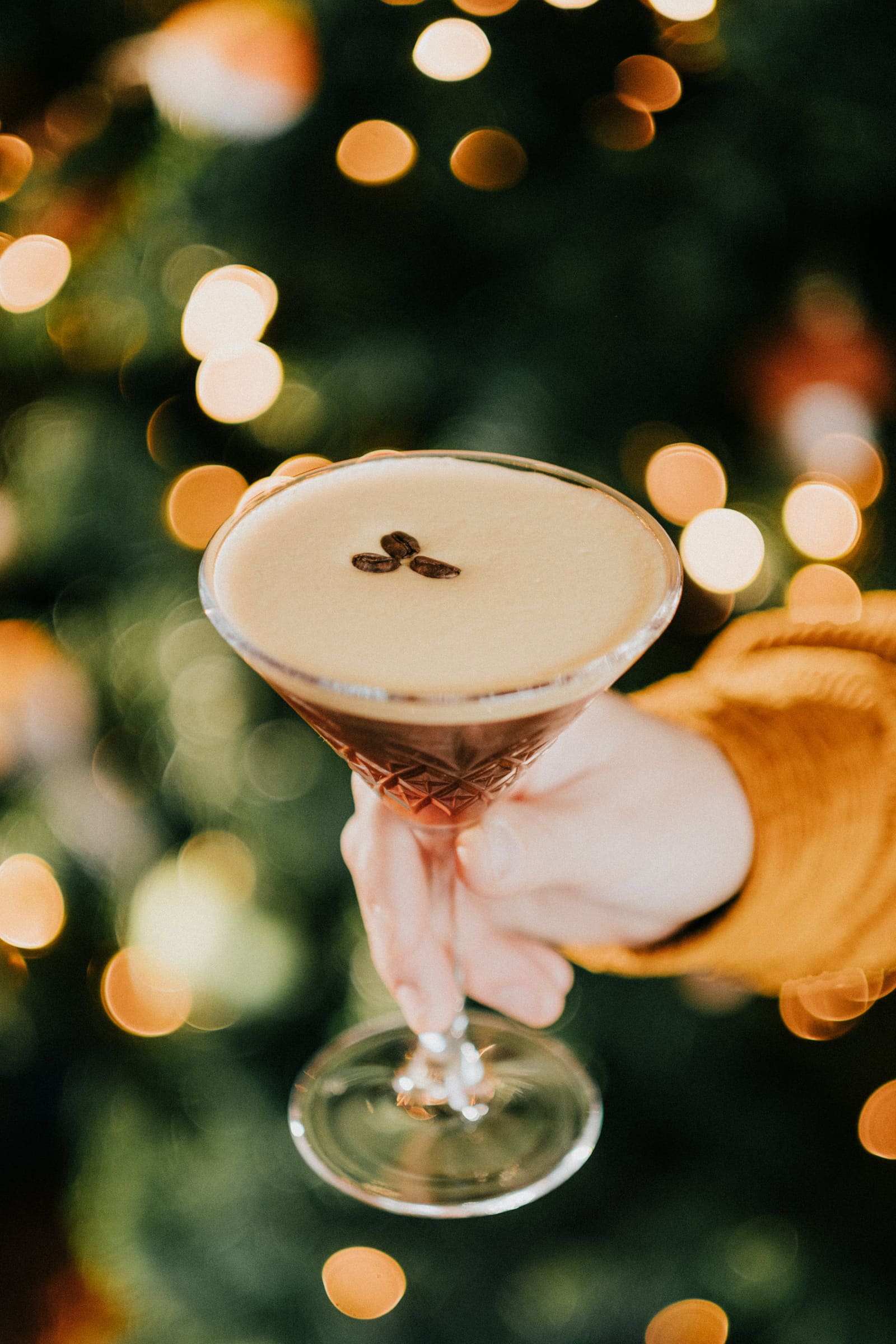 An espresso martini held up against the lights of the Christmas tree