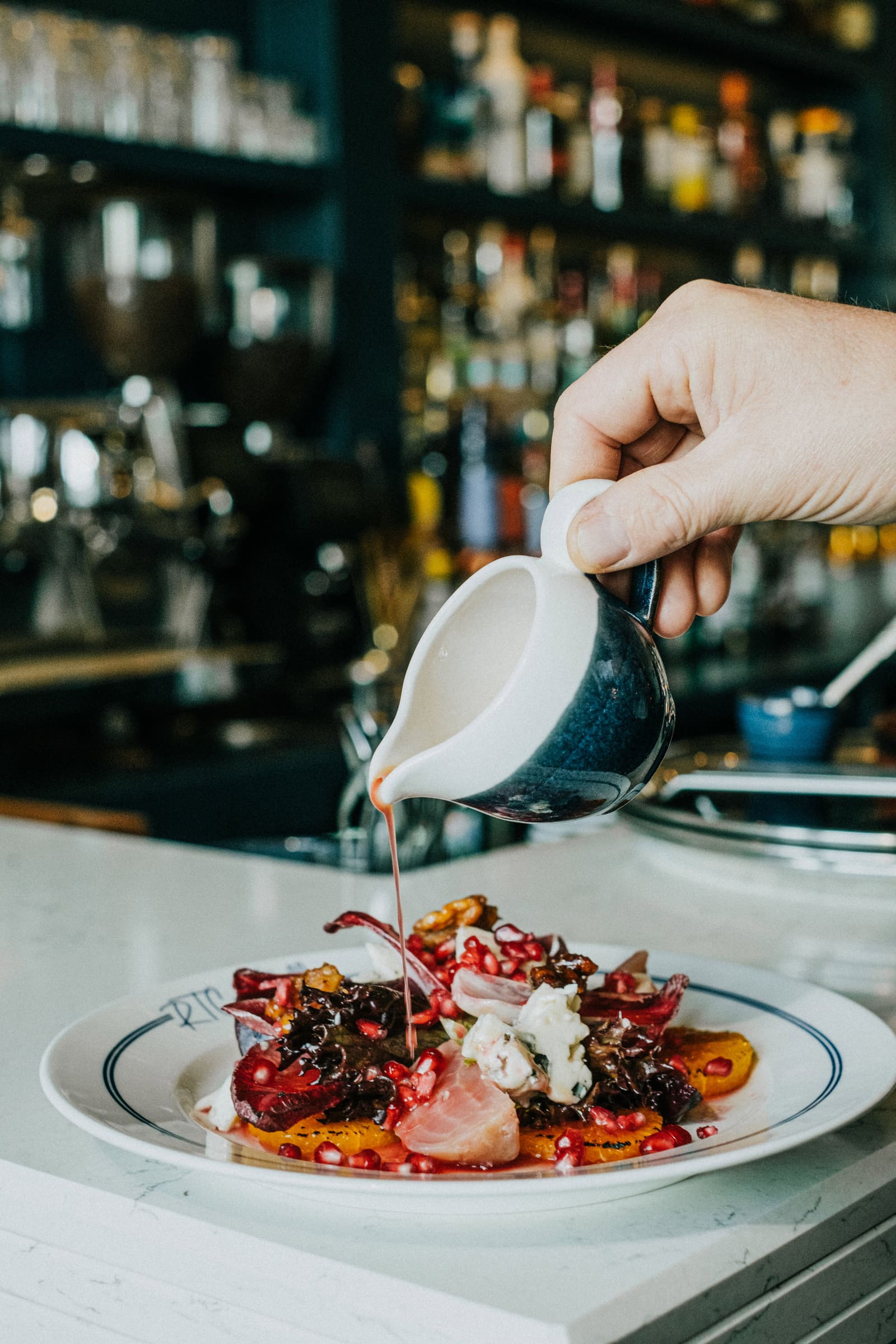 Dressing poured from a small jug over a salad at the bar