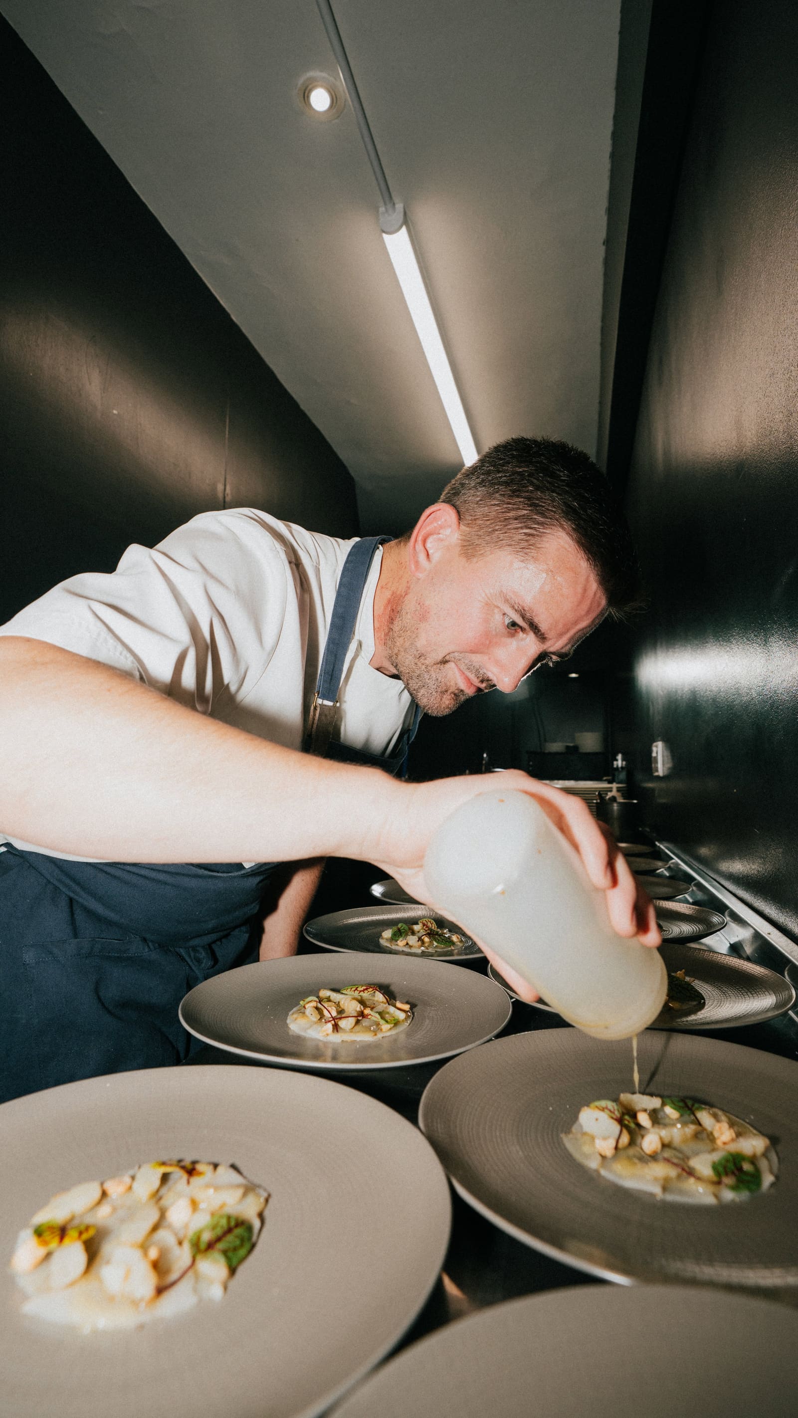 A chef finishing a plate with sauce at the pass